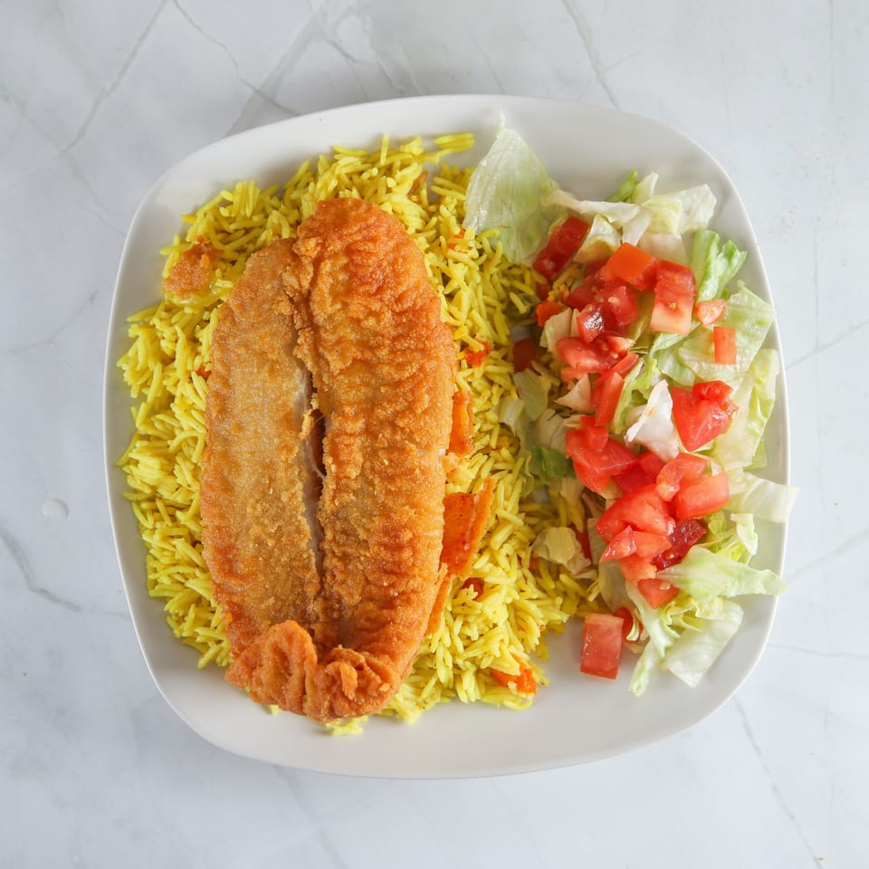 Fried fish fillet with yellow rice and a side salad of lettuce and diced tomatoes.