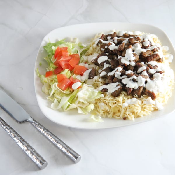 A plate of US Fried Chicken's fried chicken pieces over rice, with a side salad.