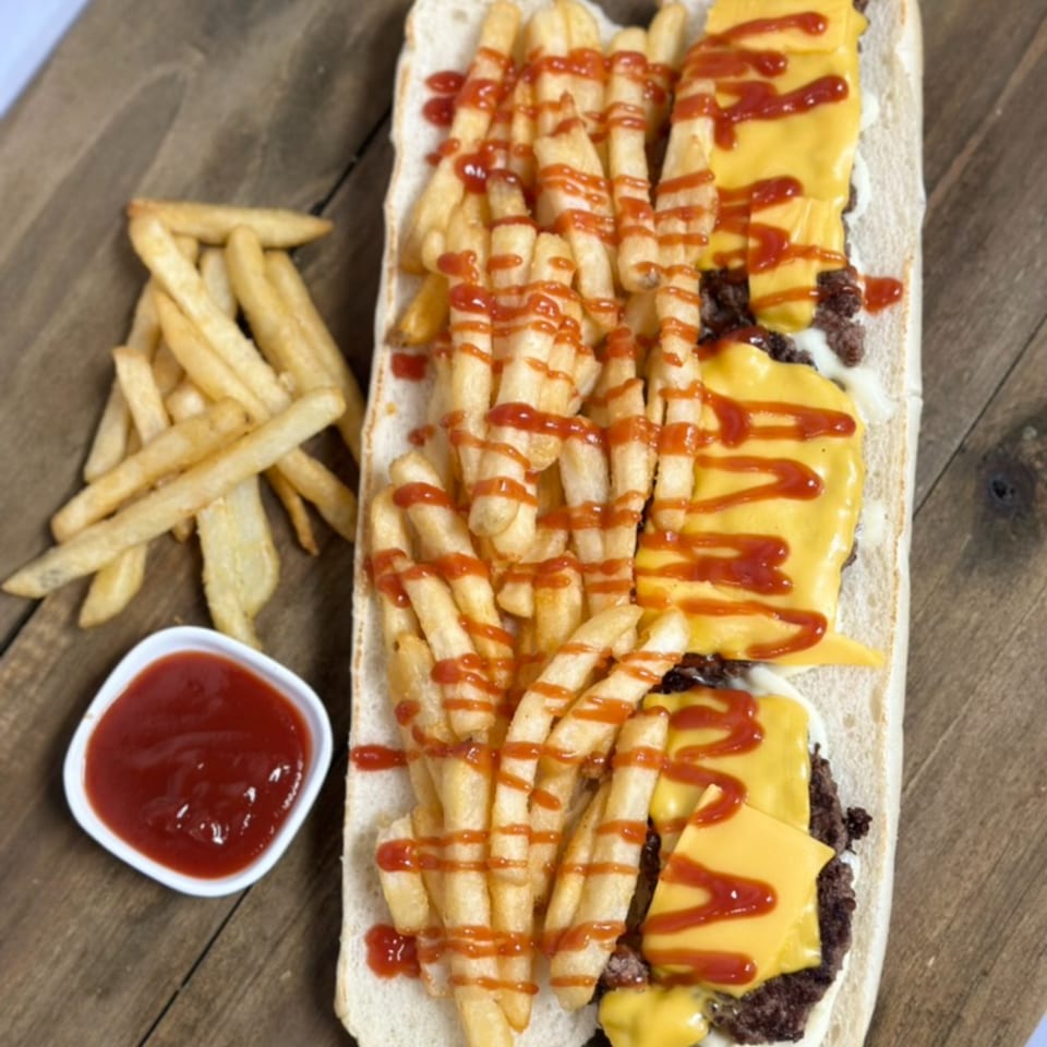 A long sandwich with ground meat, melted cheese, and french fries drizzled with ketchup.