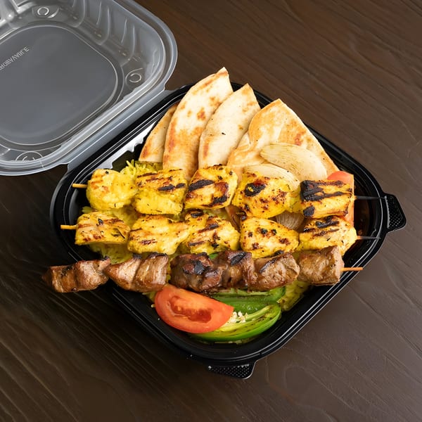 Grilled chicken and beef skewers with rice, pita bread, and vegetables in a black takeout container.