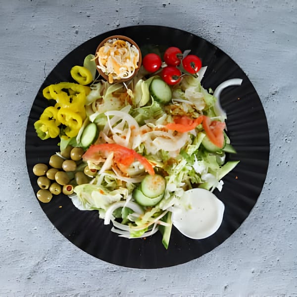Fresh garden salad with lettuce, tomatoes, cucumbers, onions, olives, and yellow peppers on a black plate.