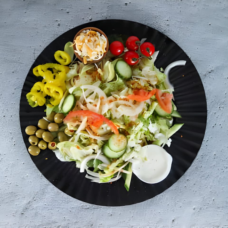 Fresh garden salad with lettuce, tomatoes, cucumbers, onions, olives, and yellow peppers on a black plate.