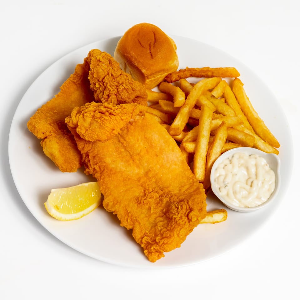 US Fried Chicken's fried fish and chicken tenders with fries, a roll, lemon, and tartar sauce.