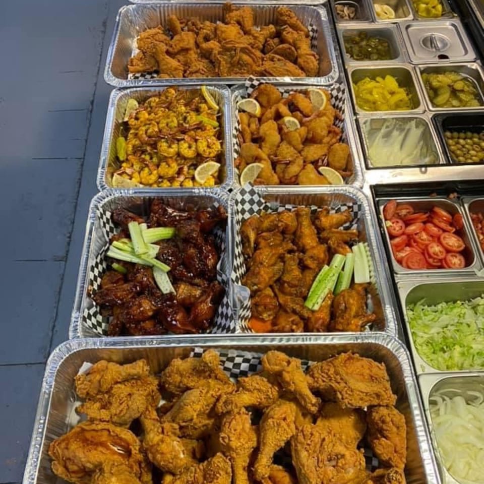 A buffet spread of US Fried Chicken, shrimp, and chicken wings, with various toppings in metal containers.