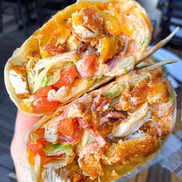 A fried chicken wrap from US Fried Chicken, cut in half, revealing chicken, lettuce, tomatoes, and sauce.