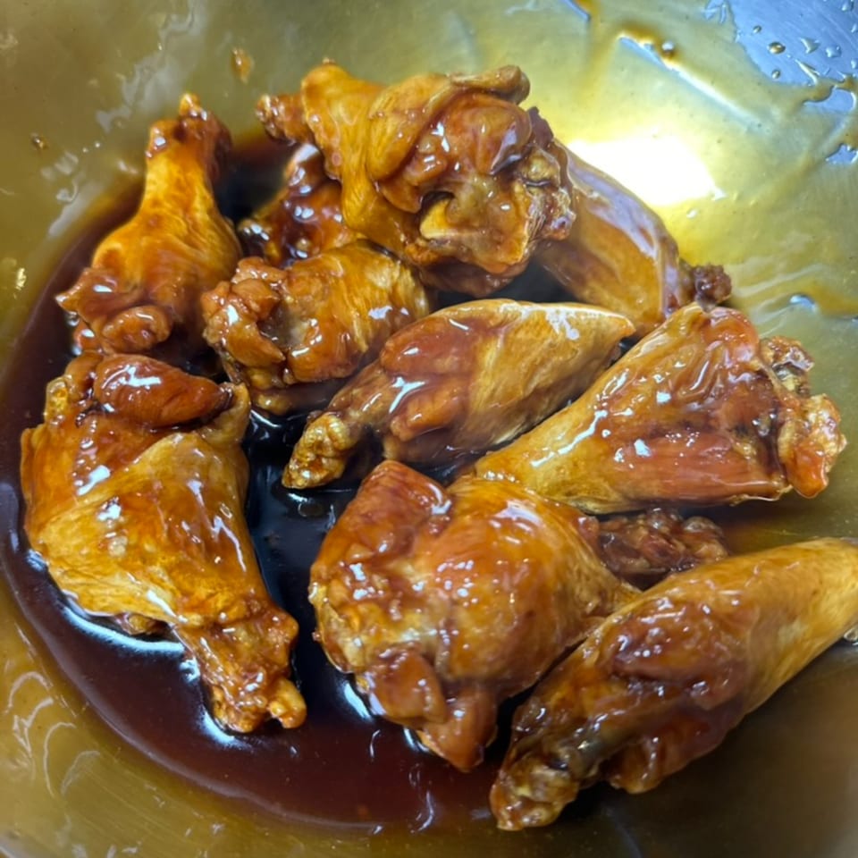 Close-up of several US Fried Chicken wings coated in a glistening, dark brown sauce.