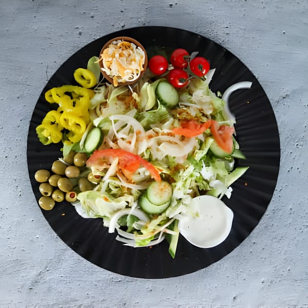 A fresh side salad with lettuce, tomatoes, cucumbers, onions, olives, and yellow peppers.