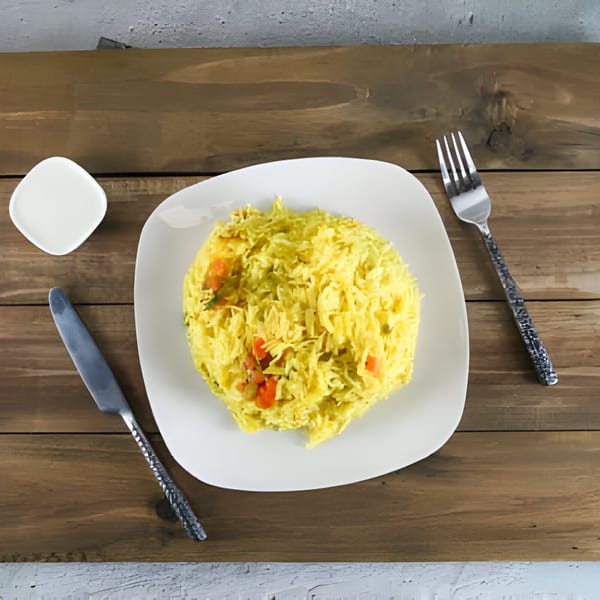A white plate of yellow rice with vegetables, a knife, fork, and small dish on a wooden table.