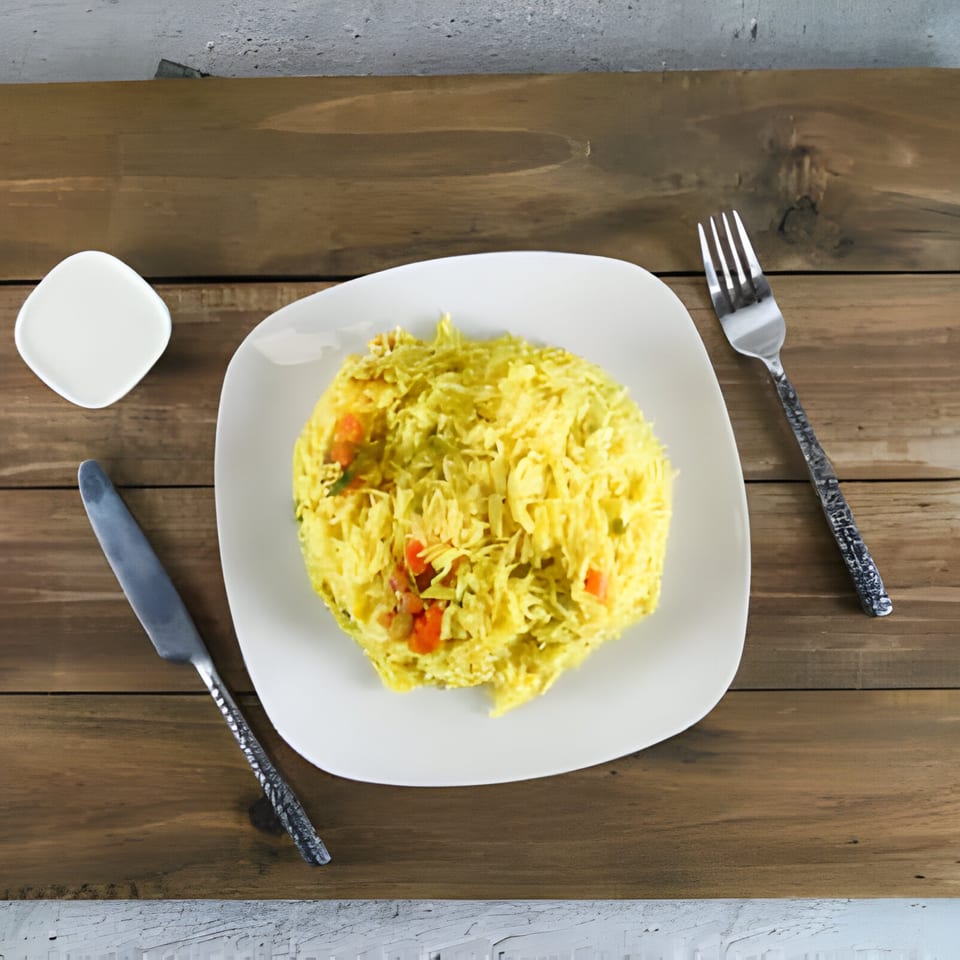 A white plate of yellow rice with vegetables, a knife, fork, and small dish on a wooden table.