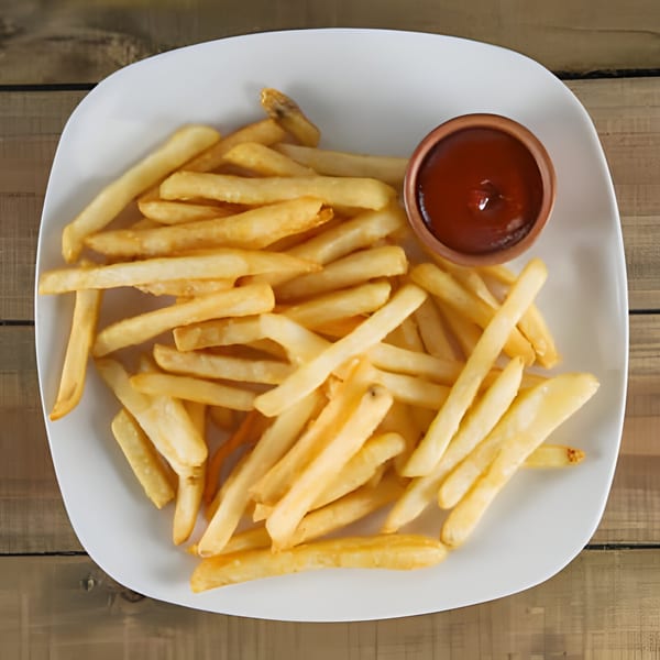 A white plate filled with golden french fries and a small cup of ketchup on a wooden table.