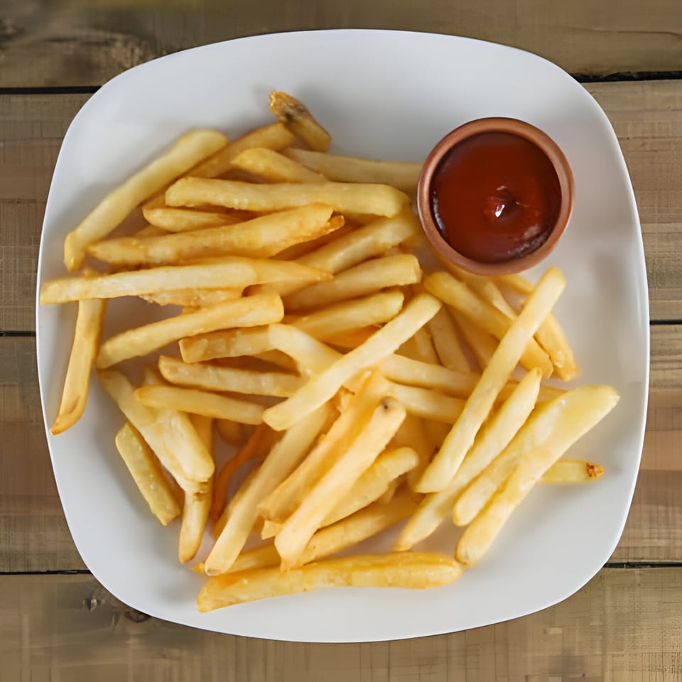 A white plate filled with golden french fries and a small cup of ketchup on a wooden table.