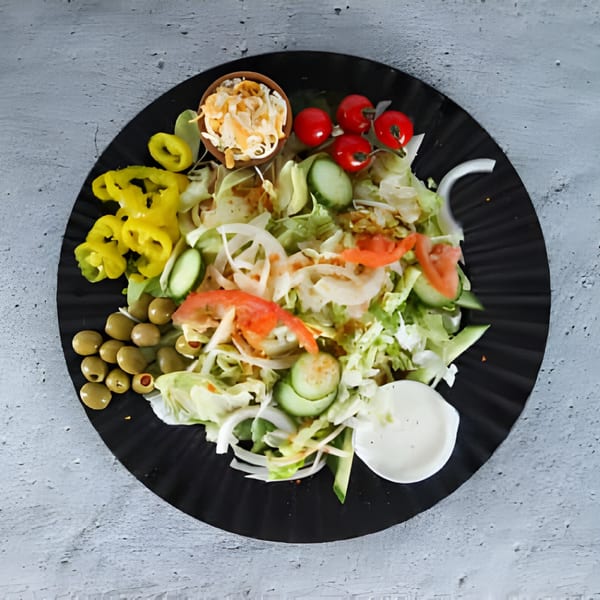 A fresh side salad with lettuce, tomatoes, cucumbers, olives, and yellow peppers on a black plate.