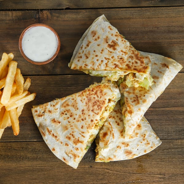 US Fried Chicken quesadillas with fries and a side of white dipping sauce on a wooden table.