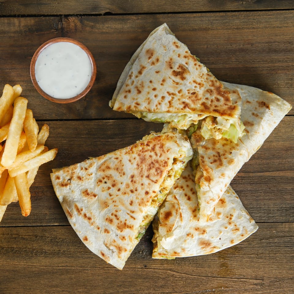 US Fried Chicken quesadillas with fries and a side of white dipping sauce on a wooden table.