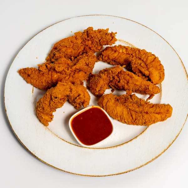 Crispy fried chicken tenders from US Fried Chicken, served with a side of red dipping sauce on a white plate.