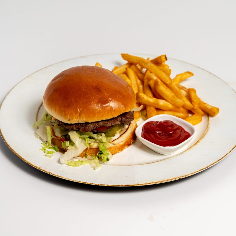US Fried Chicken burger with lettuce, pickles, and ketchup, served with golden fries on a white plate.