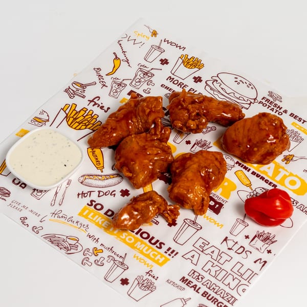 US Fried Chicken's spicy fried chicken wings with ranch dressing on a branded paper.