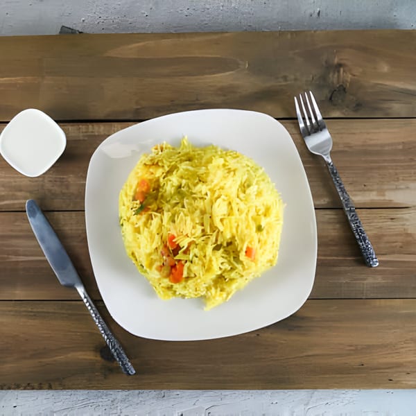 A white plate of yellow rice with vegetables, a knife, and a fork on a wooden table.
