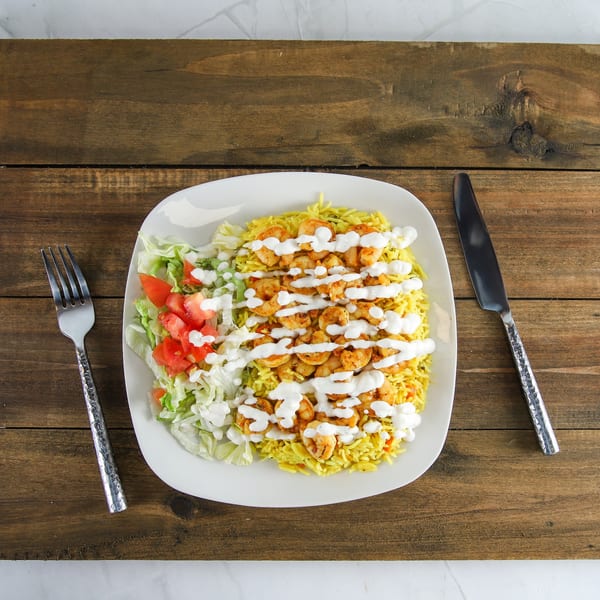 Shrimp and yellow rice with salad and white sauce on a white plate with cutlery.