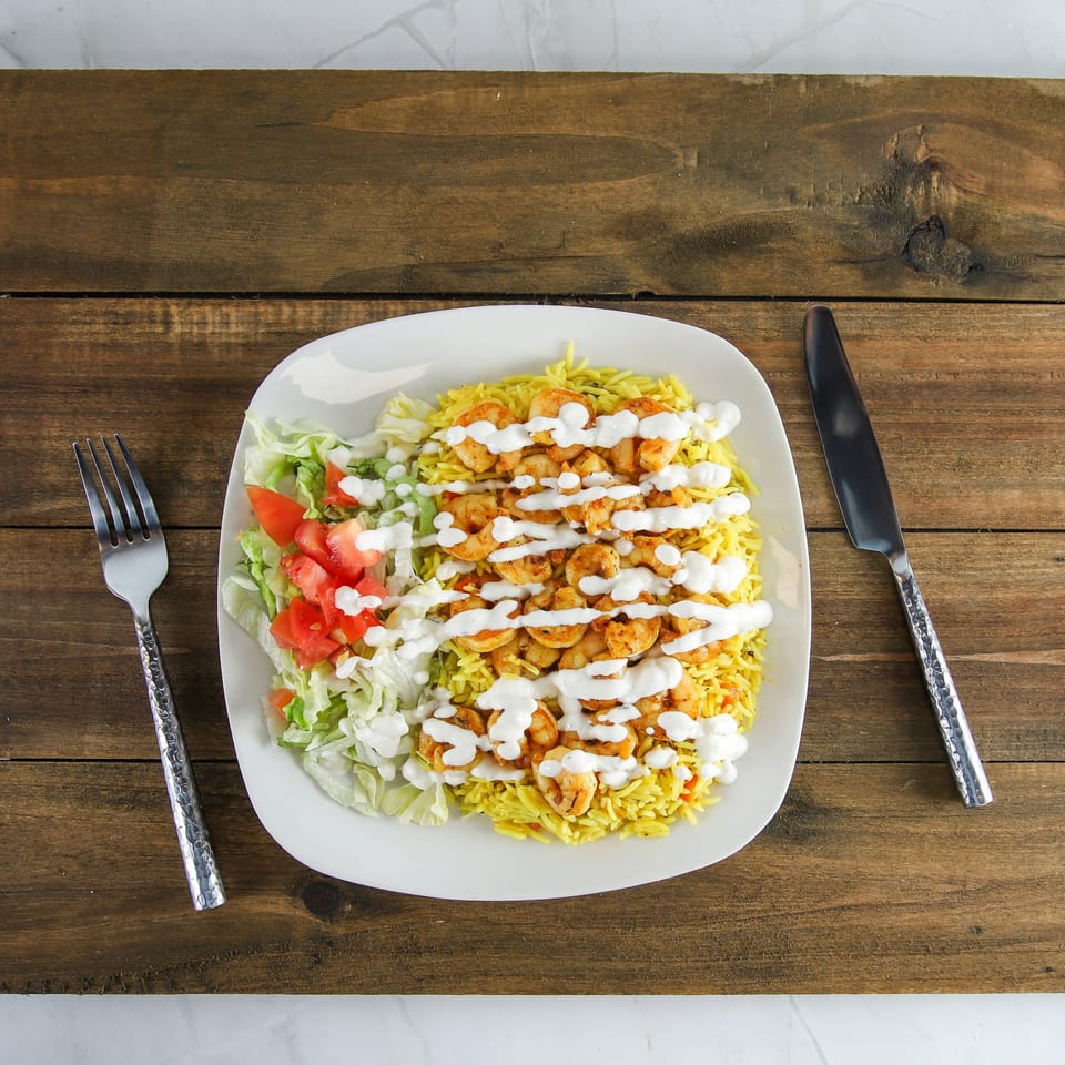 Shrimp and yellow rice with salad and white sauce on a white plate with cutlery.