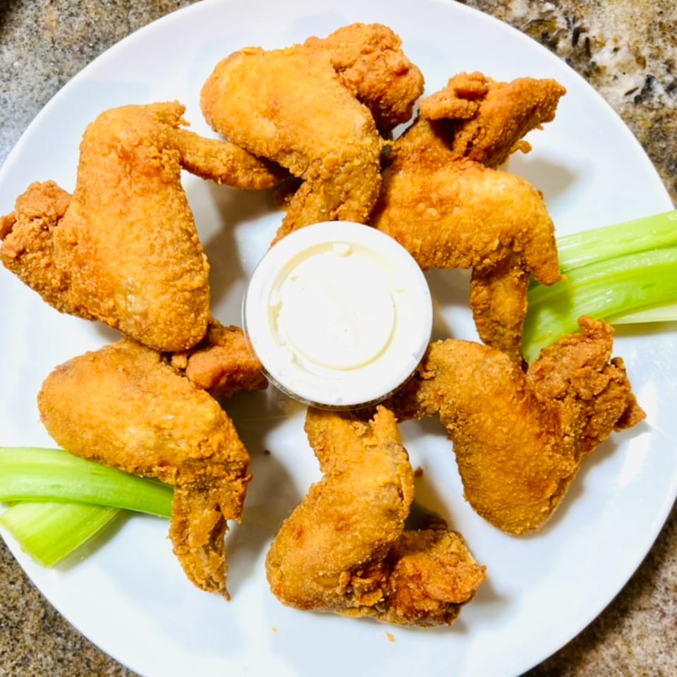 Crispy fried chicken wings with a side of ranch dressing and celery sticks on a white plate.