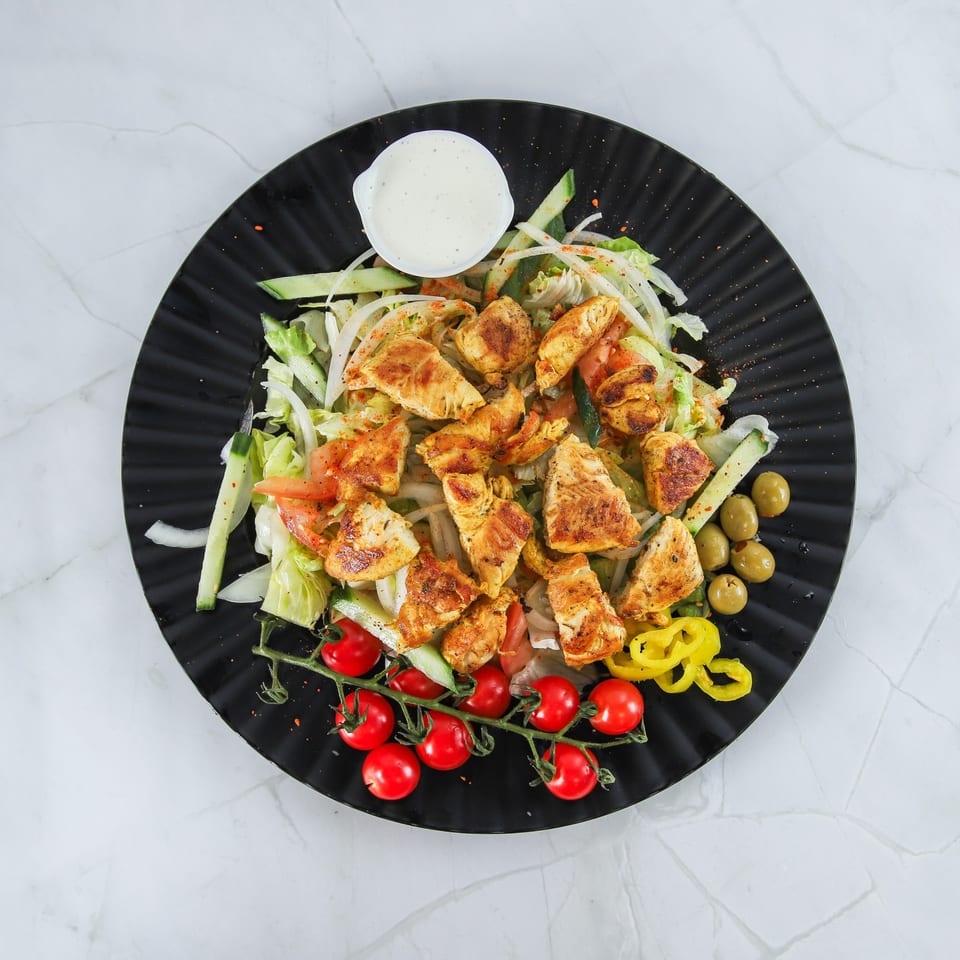 Grilled chicken salad with lettuce, tomatoes, cucumbers, olives, and a side of dressing.