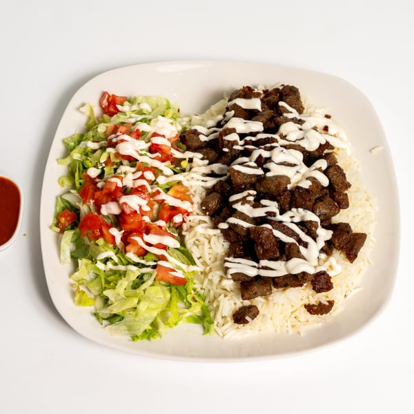 A white plate with rice, diced meat, lettuce, and tomatoes, all drizzled with white sauce.