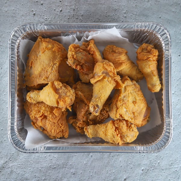 Golden-brown fried chicken pieces, including drumsticks and thighs, in a foil takeout container.