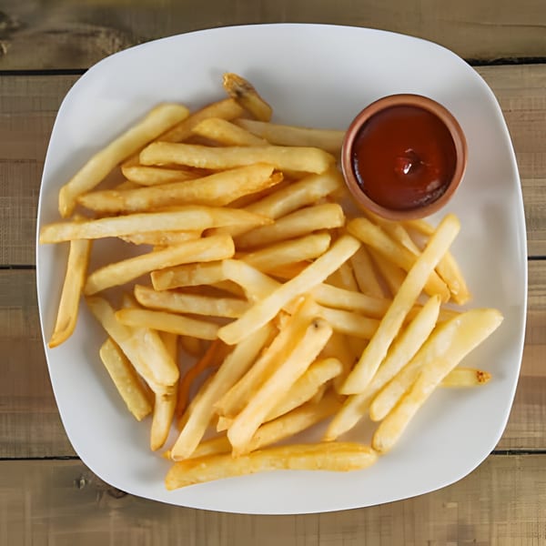 A white plate filled with golden french fries and a small cup of ketchup on a wooden table.