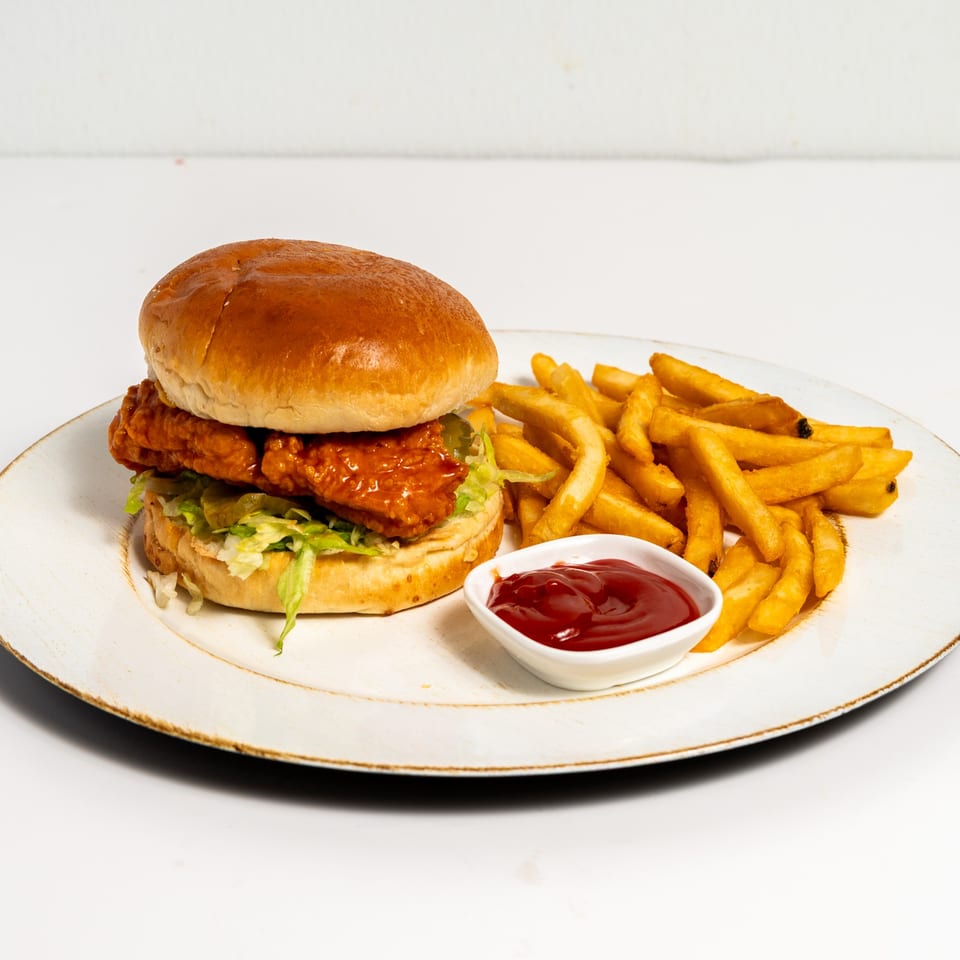 US Fried Chicken sandwich with crispy chicken, lettuce, and fries with ketchup on a white plate.