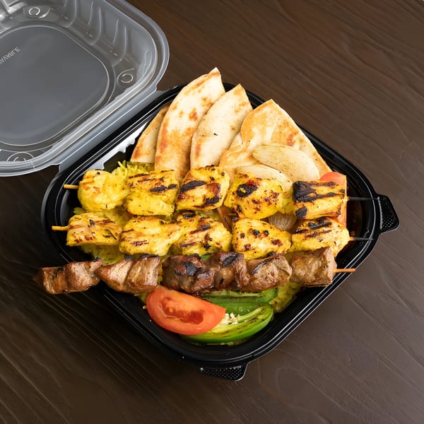 Grilled chicken and beef skewers with rice, pita bread, and vegetables in a black takeout container.