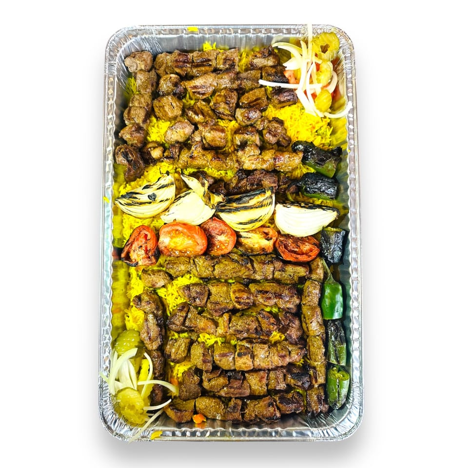 A large catering tray filled with yellow rice, grilled meat skewers, charred vegetables, and pickled onions.